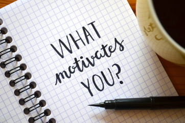 “WHAT MOTIVATES YOU?” written in notebook on desk with cup of coffee