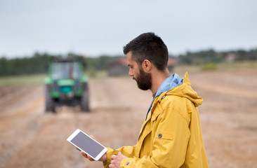 Farmer holding tablet with tractor behind
