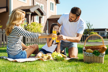 Pleasant family clinking glasses with juice on picnic