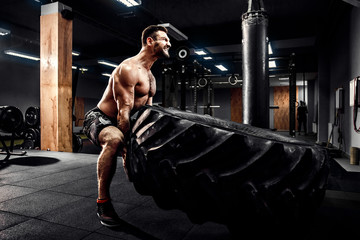 Shirtless man flipping heavy tire at crossfit gym