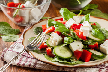 Fresh spinach salad with feta, cucumber and red paprika on a plate.