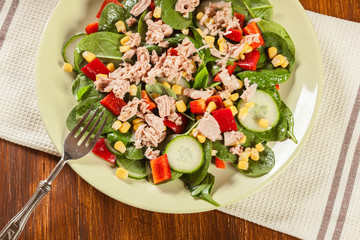 Fresh spinach salad with tuna, cucumber, corn, and red paprika on a plate