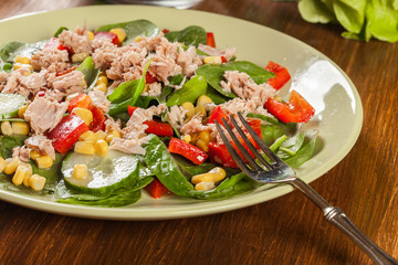 Fresh spinach salad with tuna, cucumber, corn, and red paprika on a plate