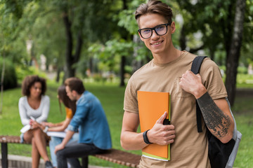 Cheerful guy holding learning material outdoors