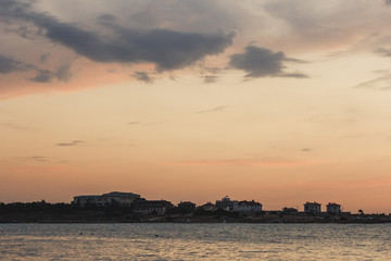 The city and the sea. On the Sunset. Contour of houses. Clouds over the sea. Evening cityscape. Sky with clouds. Background sky and urban. On the horizon line of the house. Evening. Dusk. Sea town.