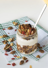 Домашняя гранола с йогуртом в стеклянной банке, на светлом фоне