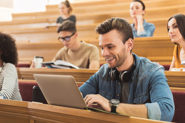 Cheerful young man studying with computer at university