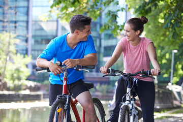 Young Couple Cycling Next To River In Urban Setting