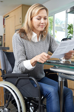 Disabled Woman In Wheelchair Reading Letter At Home