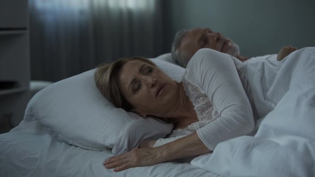 Retiree couple lying in bed awake, woman with her back to man, misunderstanding