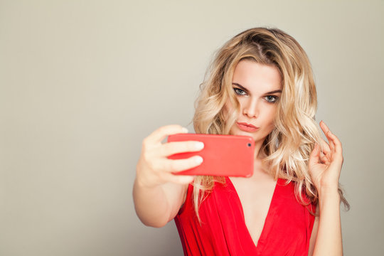 Selfie. Beautiful Blonde Woman with Makeup and Curly Hair Taking Selfie. Fashion Model in Red Cloth Using Mobile Phone