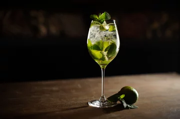  Mojitococktail met limoen en munt in longdrinkglas op een donkere stenen ondergrond © fesenko