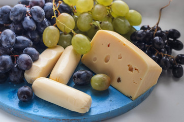 A brush of grapes in a wooden cup. two kinds of cheese