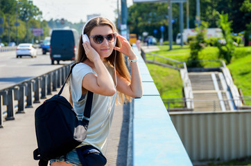 Beautiful slim stylish girl student stands on the car bridge and listens to music