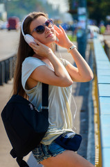 Beautiful slim stylish girl student stands on the car bridge and listens to music