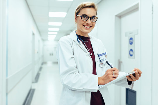 Smiling doctor standing in hospital corridor with clipboard