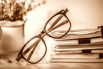 Close up black reading eyeglasses on stacking of the office paper , business working document and information data concept , vintage and retro color tone
