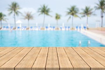 Empty wooden table in front with blurred background of swimming pool at beach,space for montage...