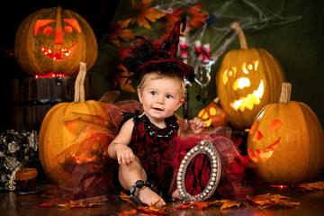 Little witch girl child laughing among pumpkins and candles.
