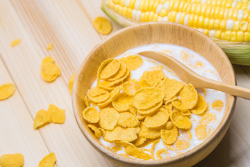 Cornflakes and milk in a wooden bowl are placed on a table with corn stalks.