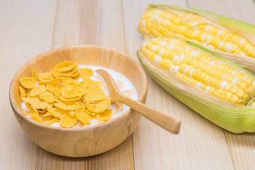 Cornflakes and milk in a wooden bowl are placed on a table with corn stalks.
