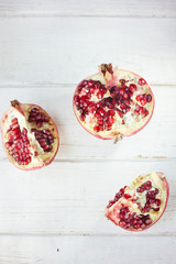 Parts of fresh pomegranate over white wooden surface.