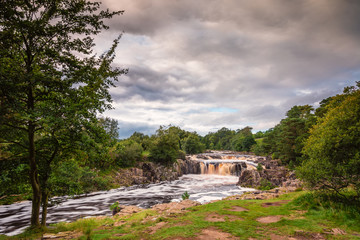 Fototapeta na wymiar Low Force Waterfall / The River Tees cascades over the Whin Sill at Low Force Waterfall, as the Pennine Way follows the southern riverbank