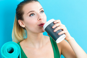 Happy young woman holding a coffee cup and a yoga mat 