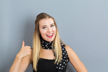 Happy young woman giving thumbs up on gray background