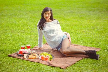 A young woman with dark hair in a white sweater at a picnic is resting on the green grass and is having a rest this afternoon. Beauty of nature and relax at sunny day