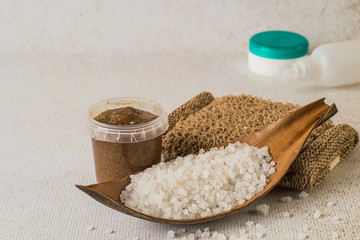  Skin care products. Sea salt, a jar with a cleansing body scrub and a loofah on a light background.