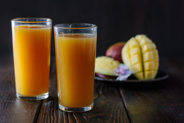 Fresh tropical mango juice on table with mango fruits on background.