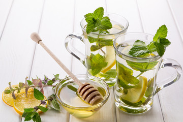 Two glass cups fresh mint tea with lemon and honey on white background.