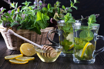 Basket with fresh green mint and two glass cups with fresh mint tea on dark  background.