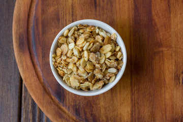 Granola or muesli in white ceramic bowl over wooden table.