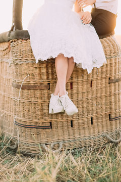 The close-up photo of the bride`s legs sitting on the straw airballoon baslet in the sunny field.