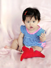 Cute baby girl with toys sit on pink planket; Baby looking straight at the camera.