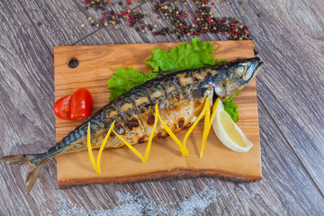 Mackerel baked on charcoal, on a wooden board with lemon and lemongrass