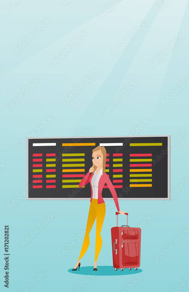 Wall mural young caucasian woman looking at departure board at the airport. passenger with suitcase standing on