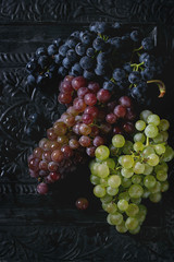 Variety of three type fresh ripe grapes dark blue, red and green. Close up over black metal ornate background. Top view