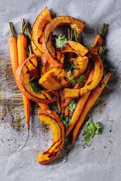 Roasted young whole carrot and sliced pumpkin with greens and sea salt on white baking paper as background. Top view with space