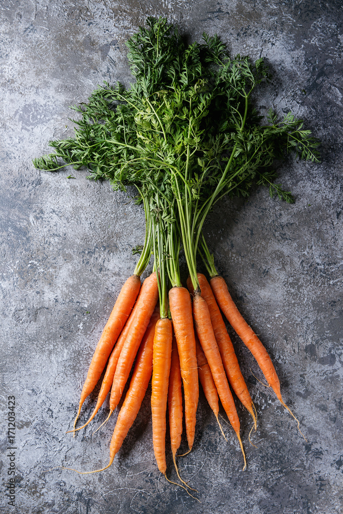 Wall mural Bundle of fresh organic carrot with haulm over gray texture background. Top view with space