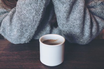 Closeup image of white hot coffee cup on vintage wooden table in cafe with woman in background
