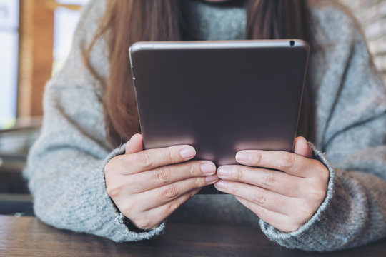 Closeup  image of a woman holding and using tablet pc sitting in modern cafe
