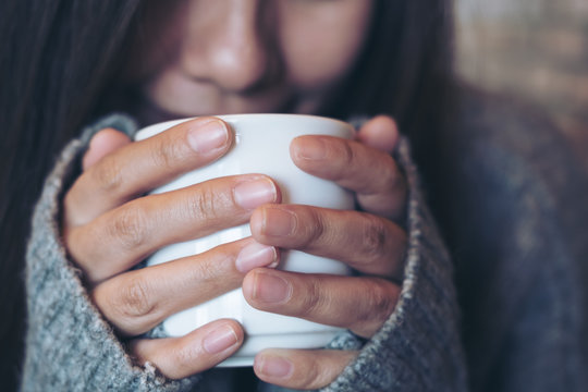 Closeup image of an Asian woman holding and drinking hot coffee in winter time