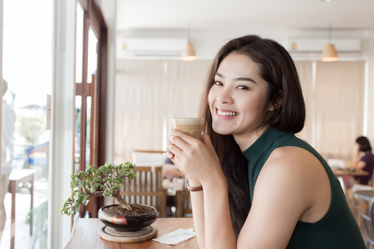Young happy Asian woman drinking coffee in the coffee shop.