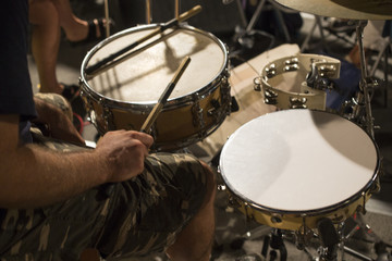 Dettaglio di un batterista mentre suona il suo strumento durante un concerto. In evidenza le bacchette e i tamburi centrali.