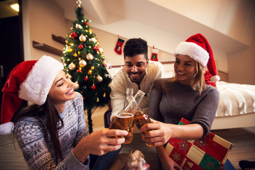 Charming happy young friends are celebrating Christmas with drinks.