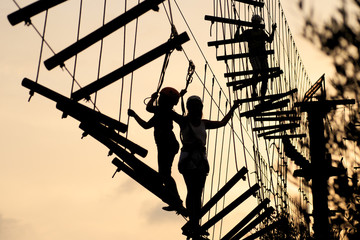 Silhouettes of people a walking on a rope ladder, a rope park. Family hobby