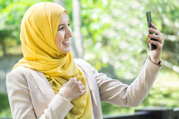 Happy young muslim woman holding a phone and taking selfie.